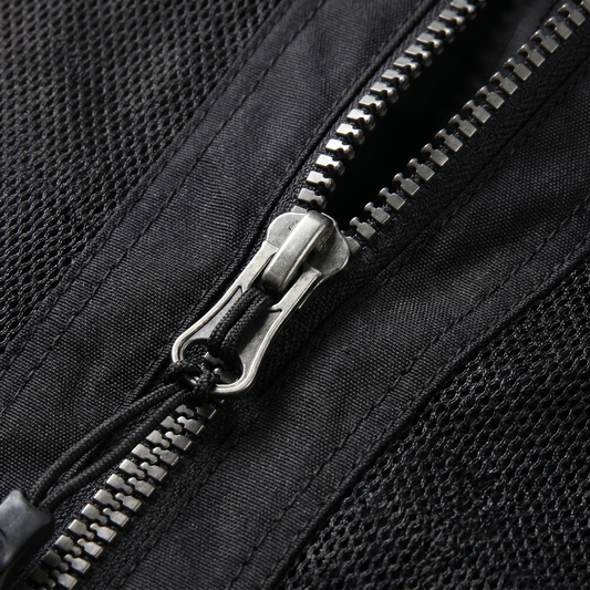 Nahaufnahme des metallenen Reißverschlusses einer schwarzen Mesh-Jacke mit Schieber, geflochtenem Zugband und grobmaschigem Netzgewebe links und rechts der Zahnreihe